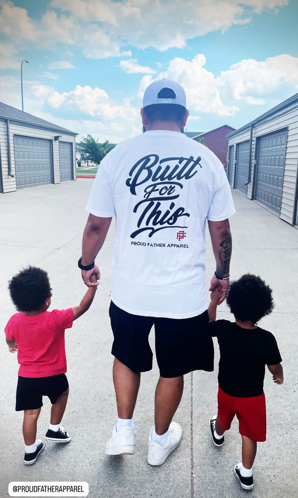 Man wearing a white t-shirt with text, holding hands with two children on a sidewalk.