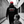 Man wearing a black hoodie with text and a red cap, walking with a child in an urban setting.